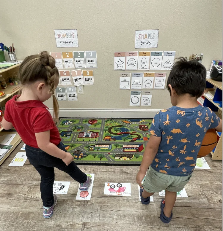 Preschool students standing on learning cards with shapes and numbers in child care classroom