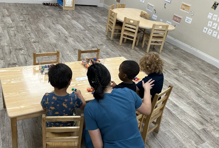 Daycare teacher helping preschool children with colorful alphabet puzzle in classroom